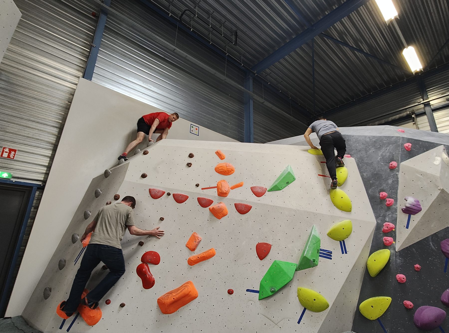 Drie collega's klimmen tegelijk op een grote boulderwand met gekleurde grepen.