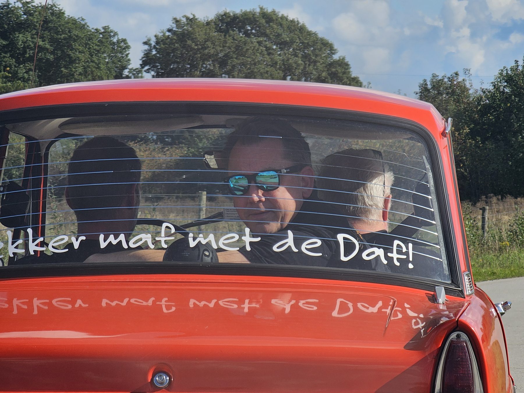 Collega's rijden in een rode Daf met op de achterruit 'Lekker maf met de Daf!'.