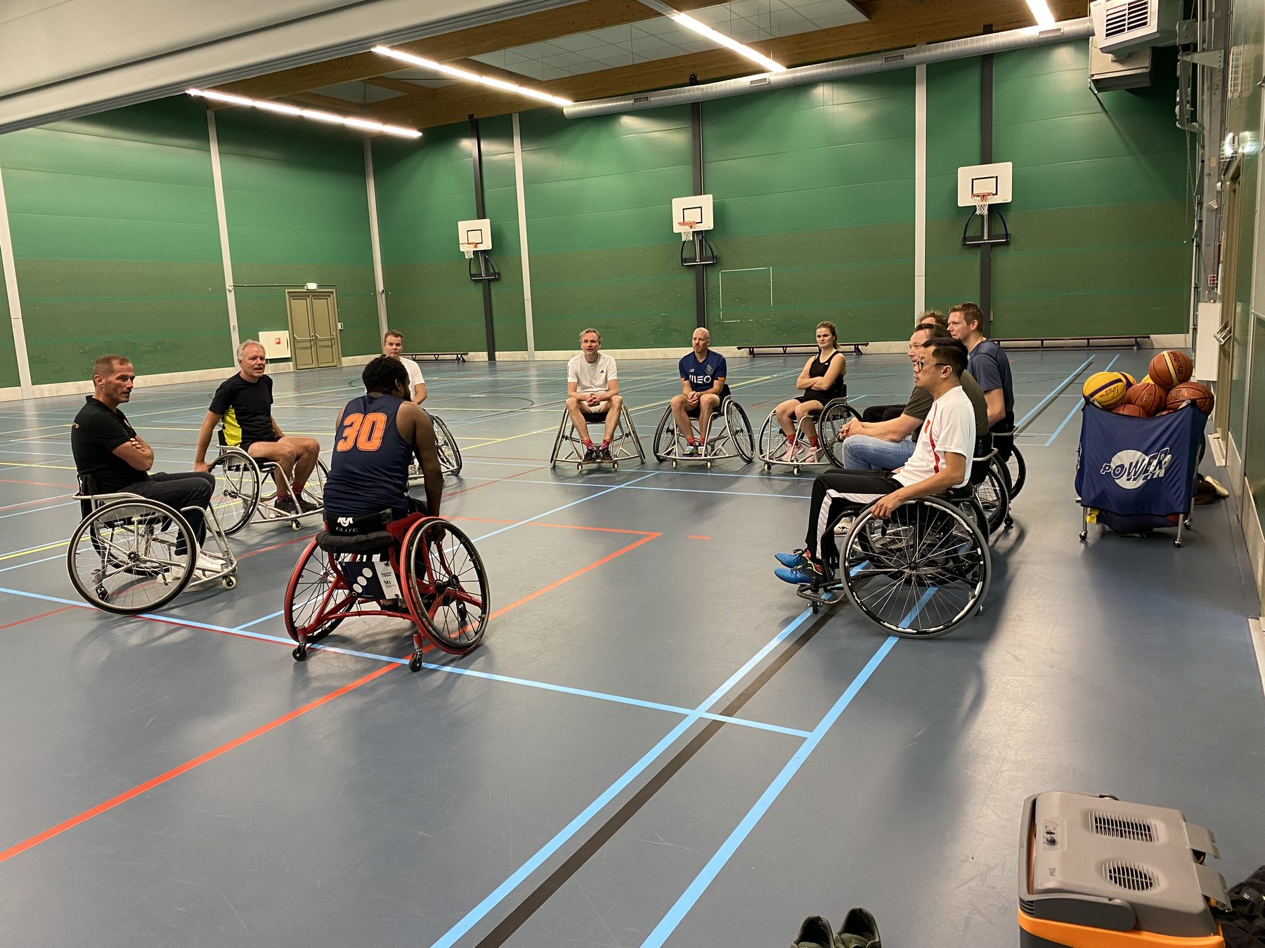 Collega's spelen rolstoelbasketbal in een sporthal.