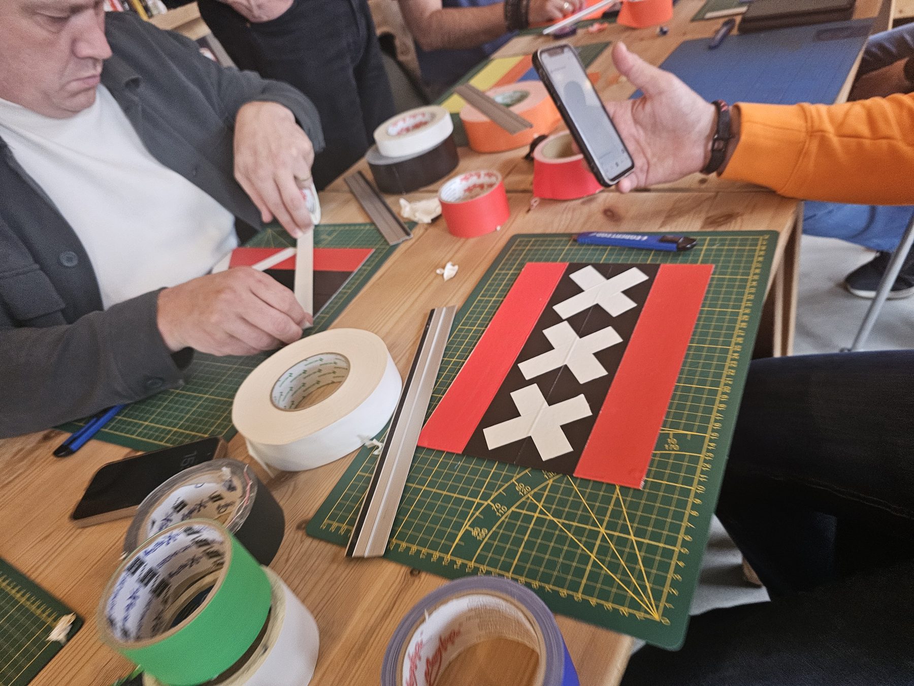 Handen met rollen gekleurde tape maken een Amsterdamse vlag op een snijmat.
