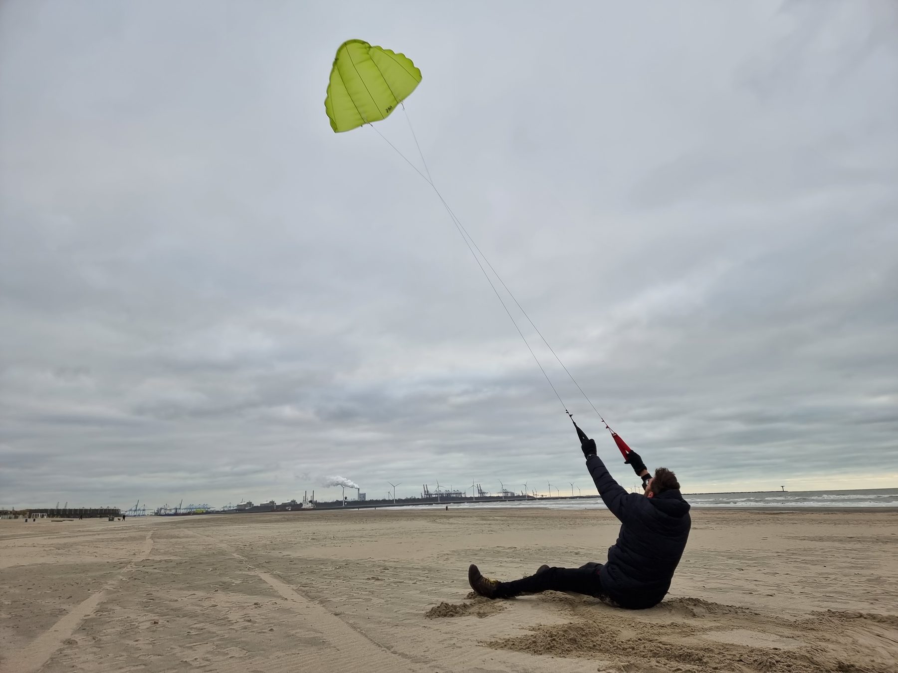 Een collega zit in het zand en houdt een groene vlieger in bedwang op het strand van Hoek van Holland.