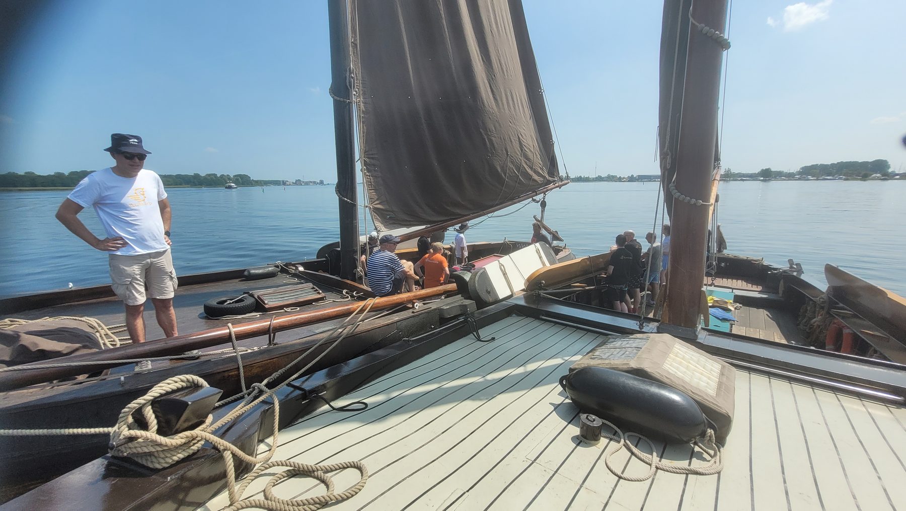Collega's aan boord van een traditioneel zeilschip met bruin zeil op het water.