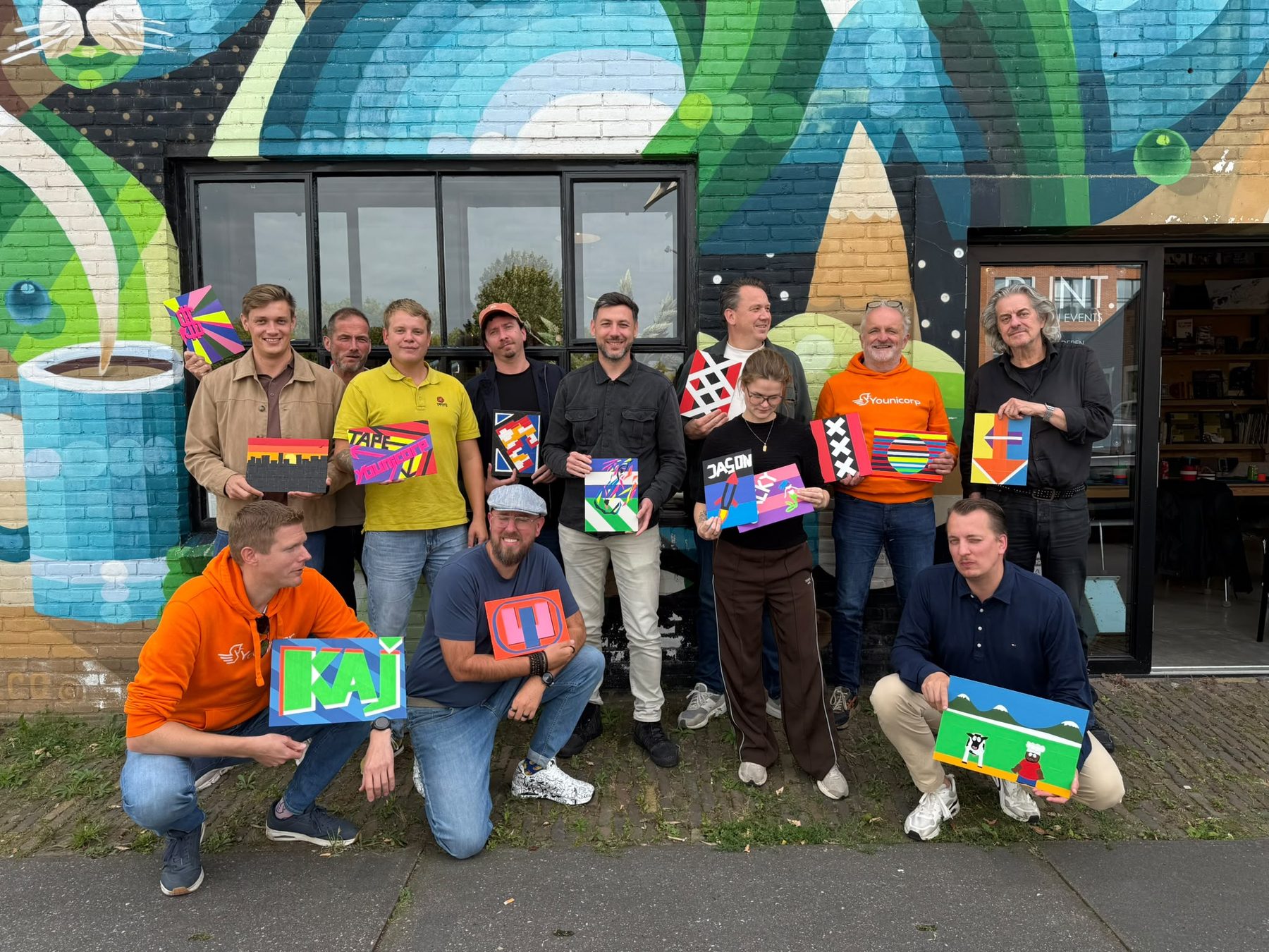 Het team poseert met zelfgemaakte tape-art voor een kleurrijke muurschildering.