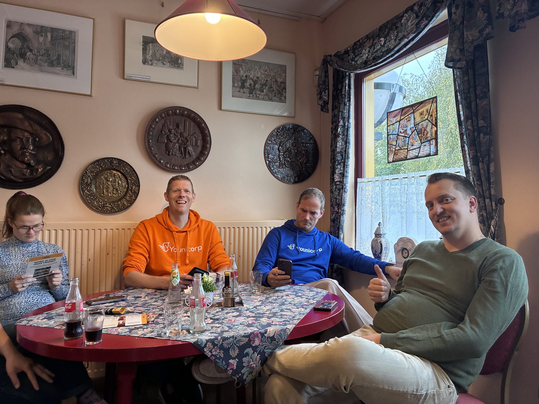Collega's in Younicorp-hoodies aan tafel in een theetuin, met borden aan de muur.