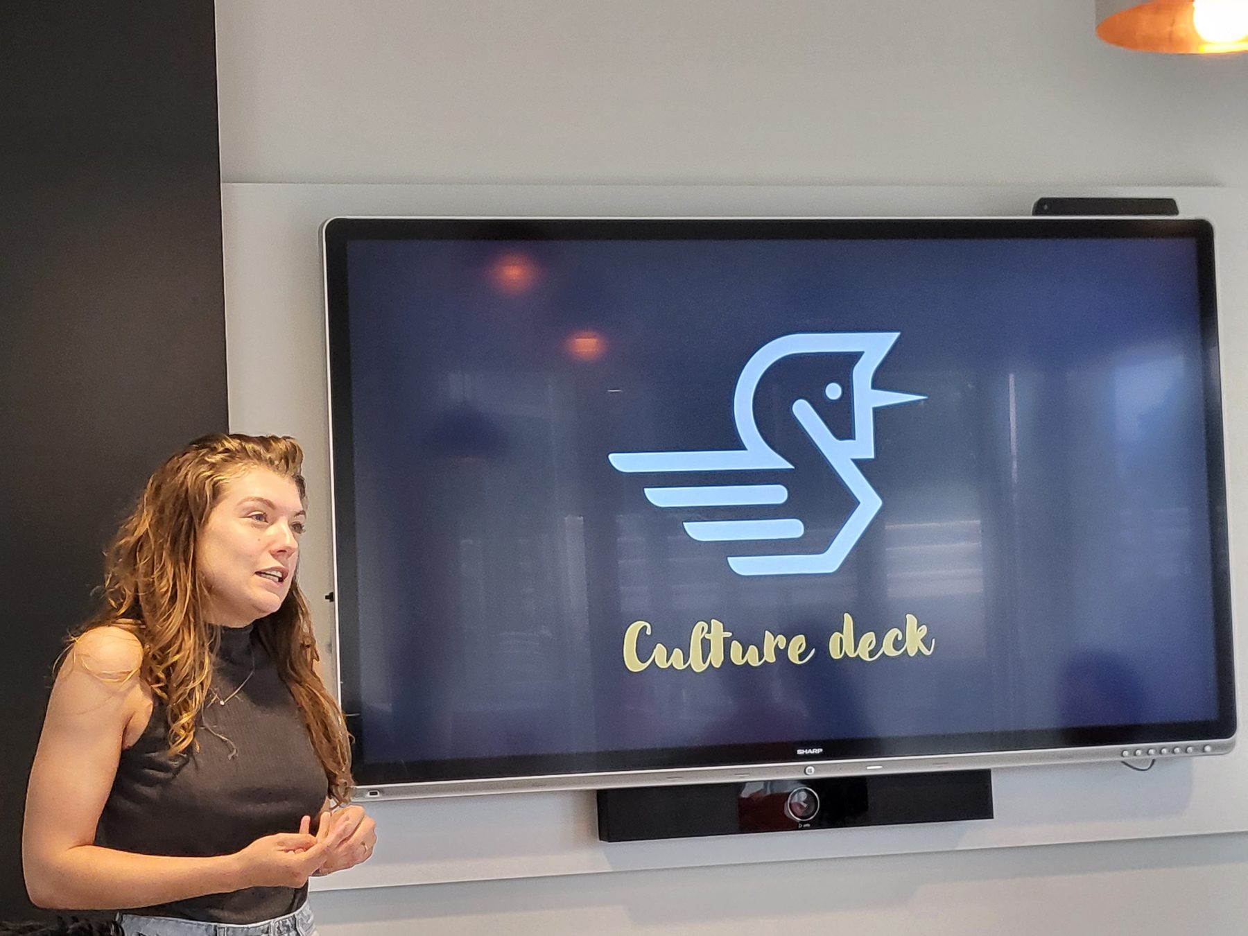 Een collega presenteert het Younicorp culture deck; op het scherm staat het beeldmerk.